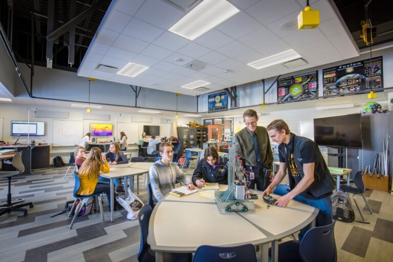 Students and a teacher work on a robotics project in an open STEM lab with flexible seating and tables at DeForest Area High School