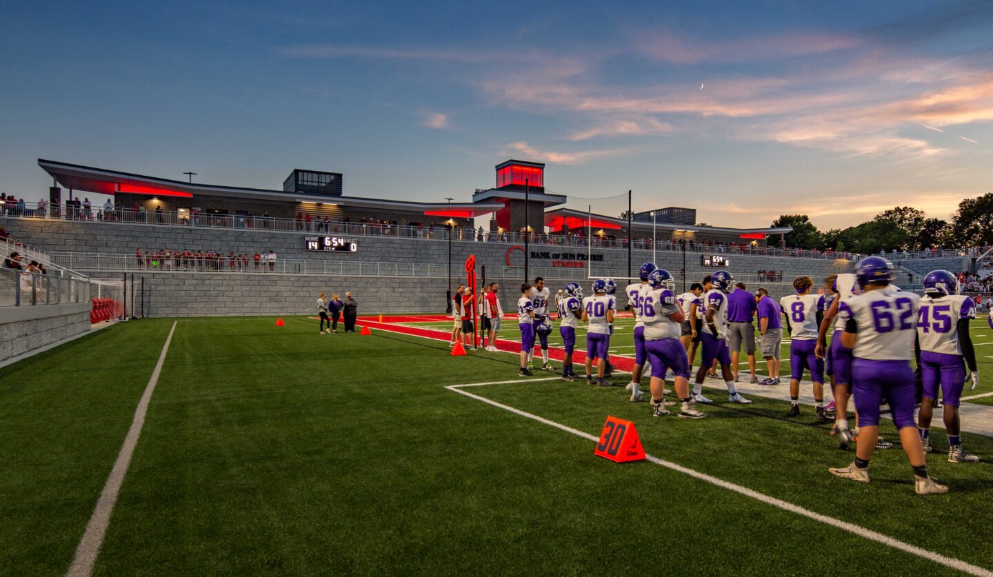 Football players at the sidelines at dusk with a plaza overlook in the background