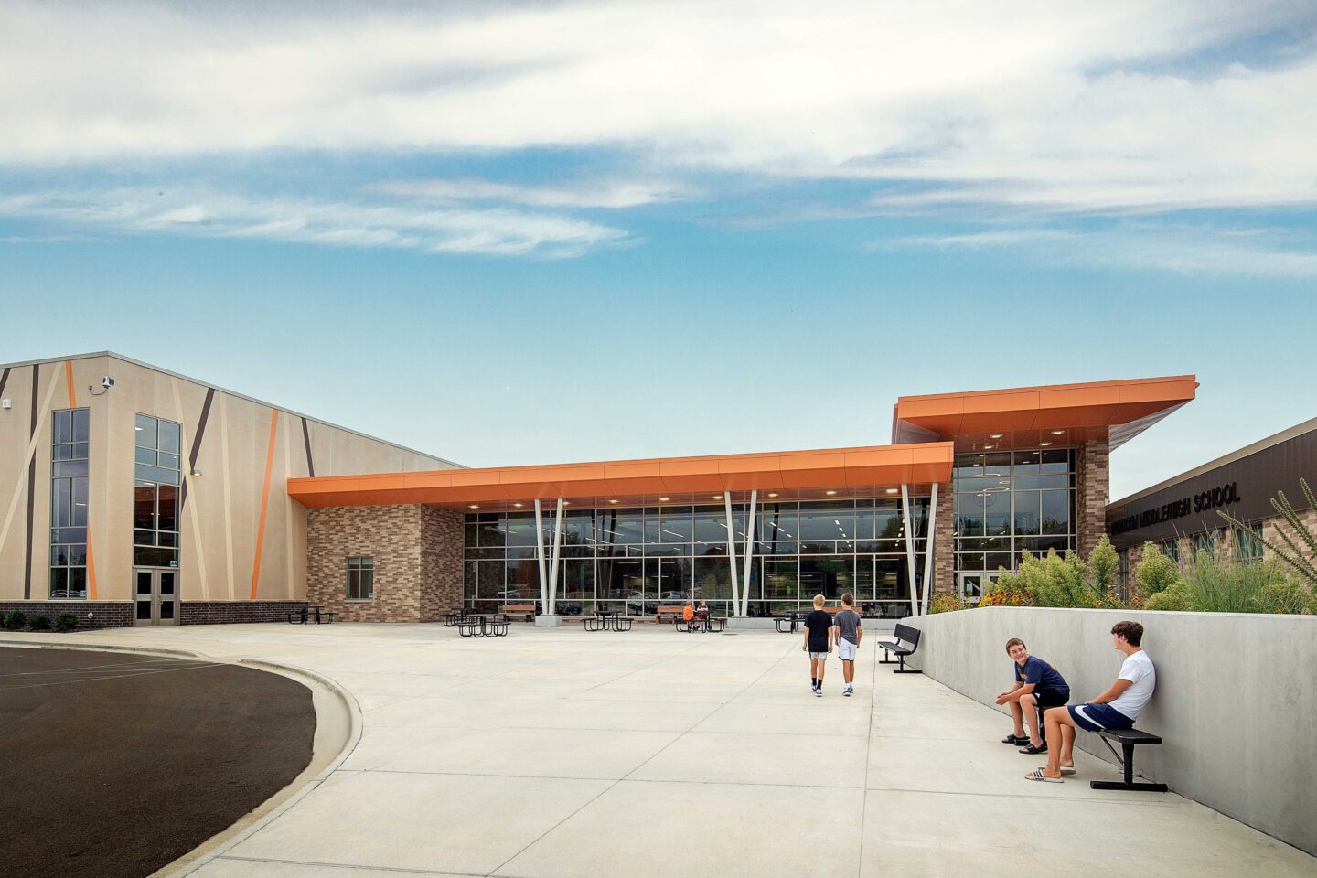 A large plaza with students leads into a modern school entrance