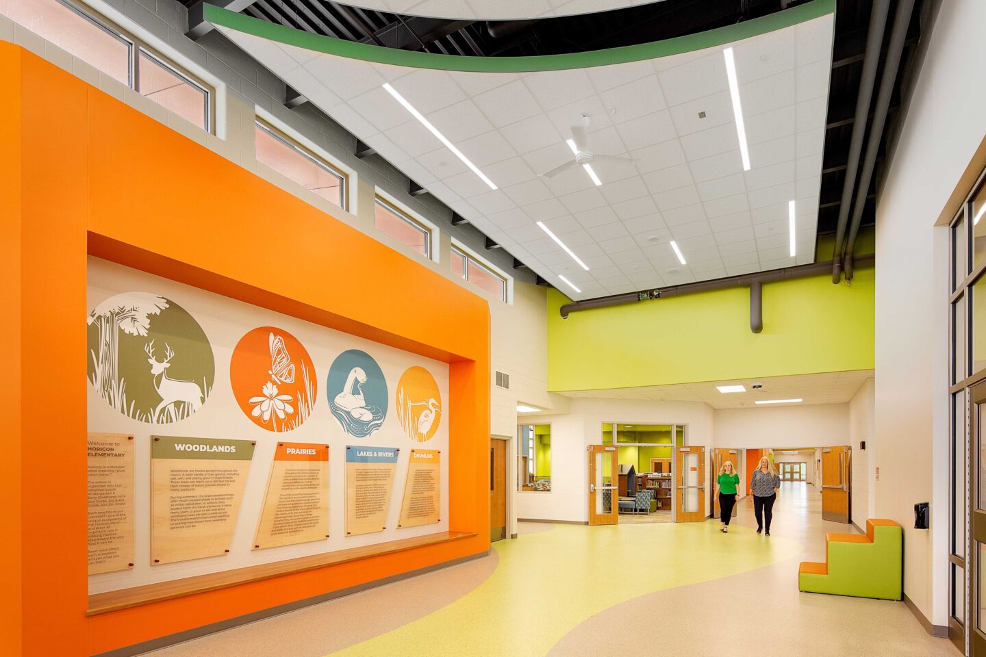 An open and brightly colored school hallway with a wall mural featuring natural elements