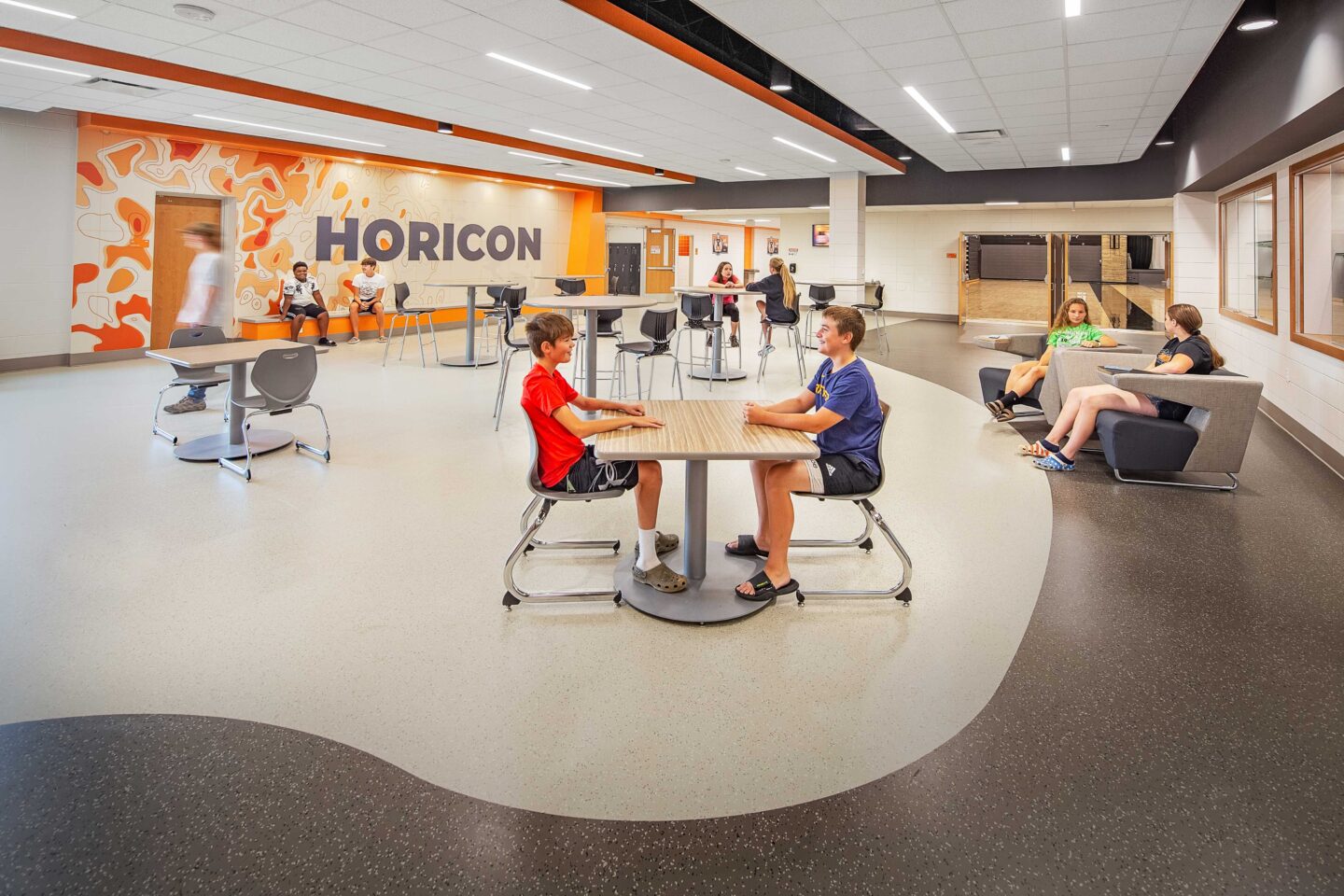 Students sit in a commons area with a large mural in the background