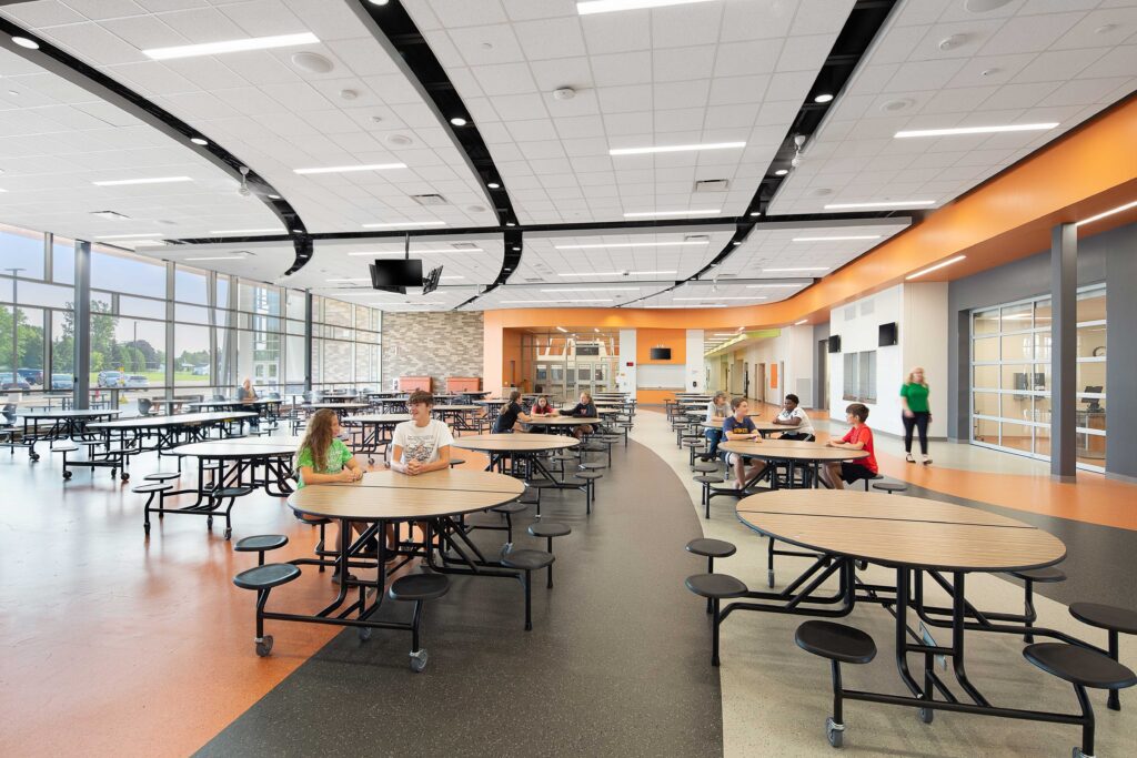 Students sit at tables in a cafeteria with a large window wall