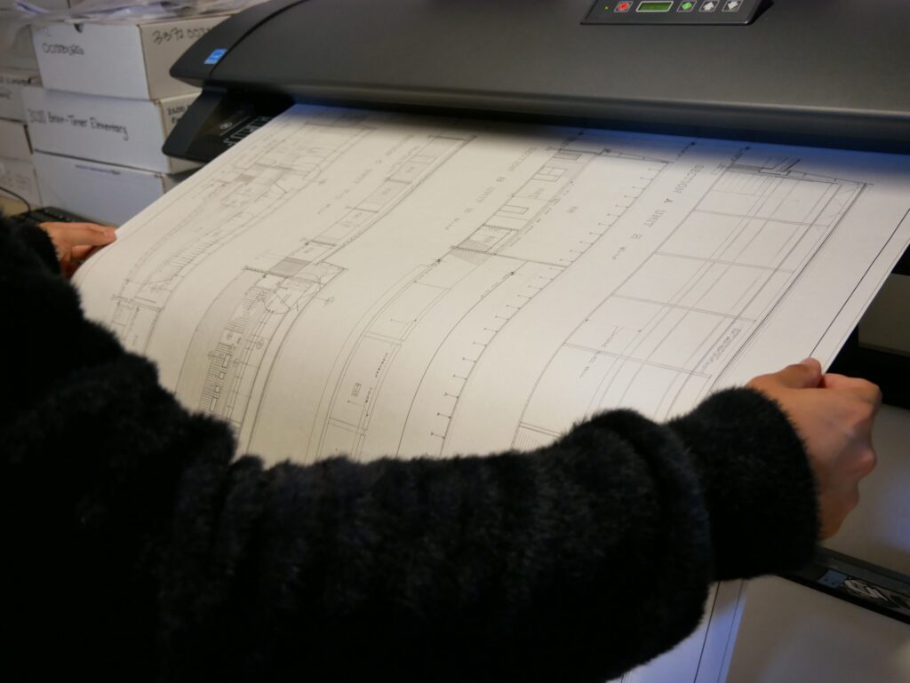 A person holds large architectural plans as they are fed into a scanner