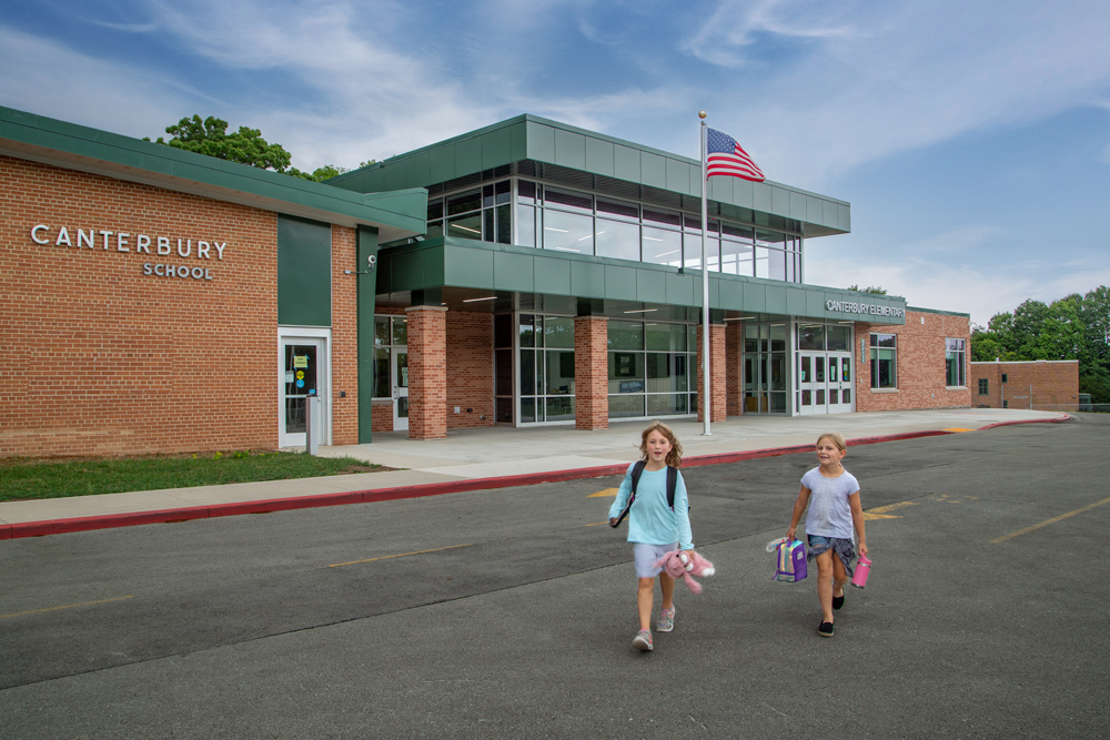 Students walk near an updated entrance with school colors and large windows at Greendale's Canterbury Elementary School