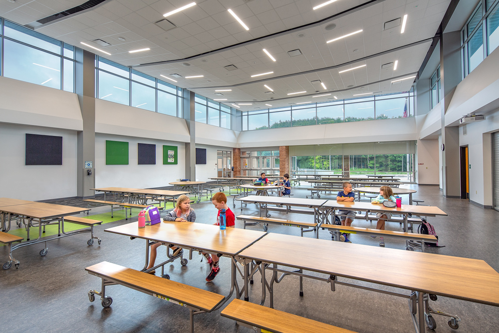 A high ceiling is lined with windows on multiple sides in a colorful, open cafeteria space at Canterbury Elementary in Greendale