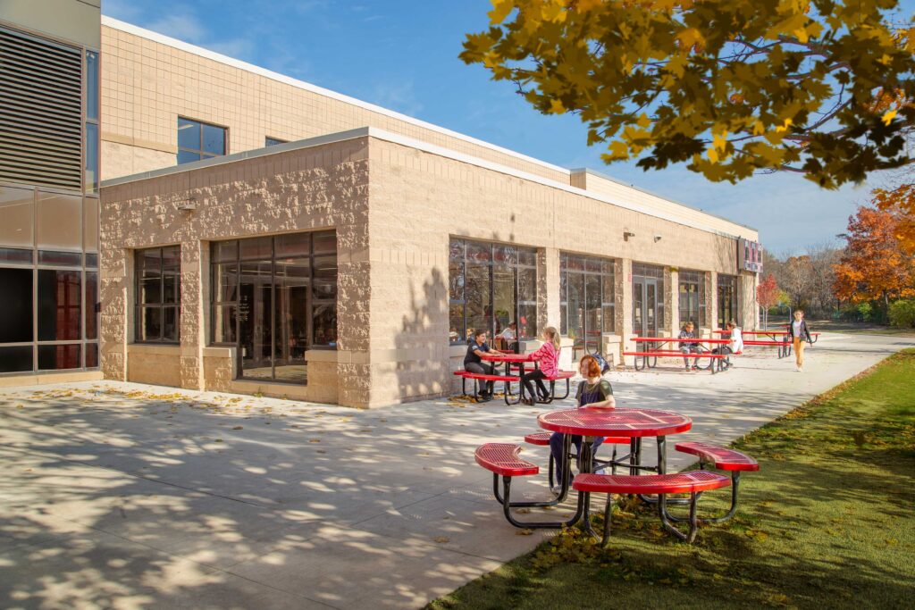 A window-lined cafeteria juts out from the main building as students sit outside at Asa Clark Middle School