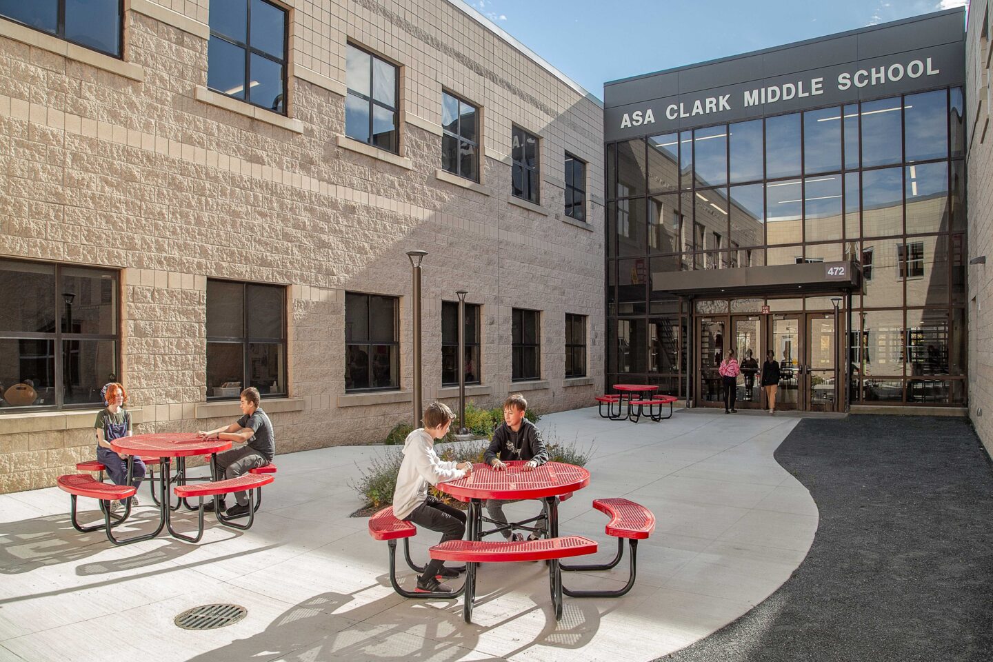 Students at red cafeteria tables eat and talk in an outdoor courtyard at Asa Clark Middle School