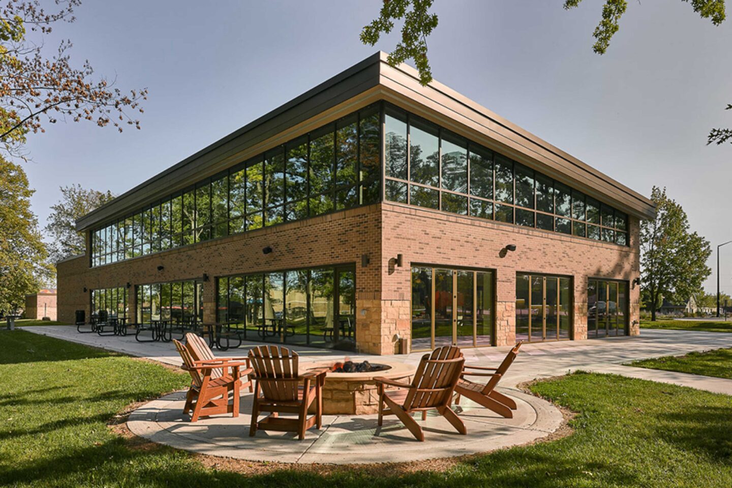 Adirondack chairs circle an outdoor fire pit with a two-story, windowed building in the background