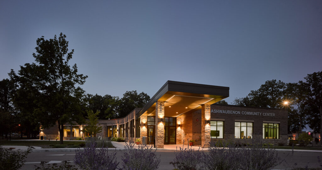 A twilight view of an upswept entryway connecting to a wide, low building