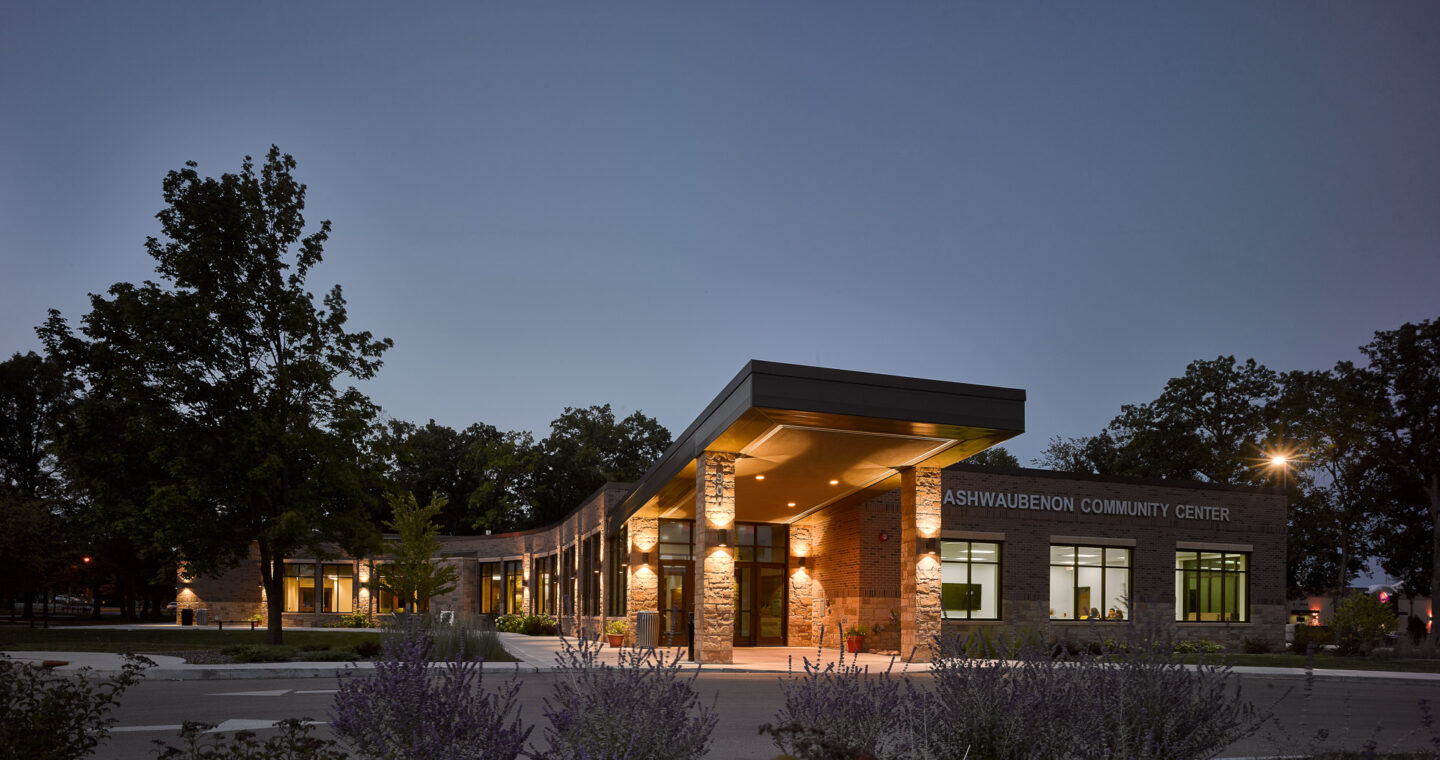 A twilight view of an upswept entryway connecting to a wide, low building