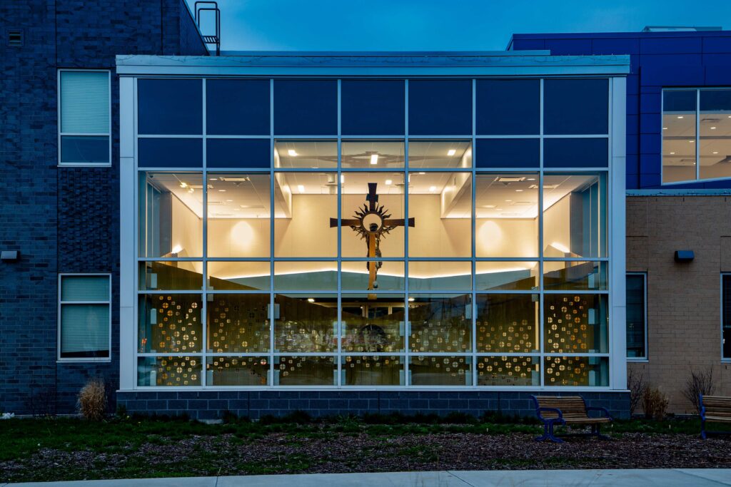 Exterior photo taken at dusk of the chapel with lights on inside, highlighting the cross.