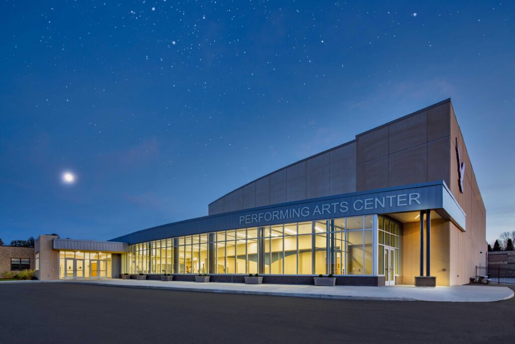 Exterior view of a curved, windowed facade on a performing arts center underneath a starry sky