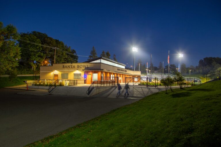 Night view of the athletic center building, with a partial view of the field and grandstands in the background