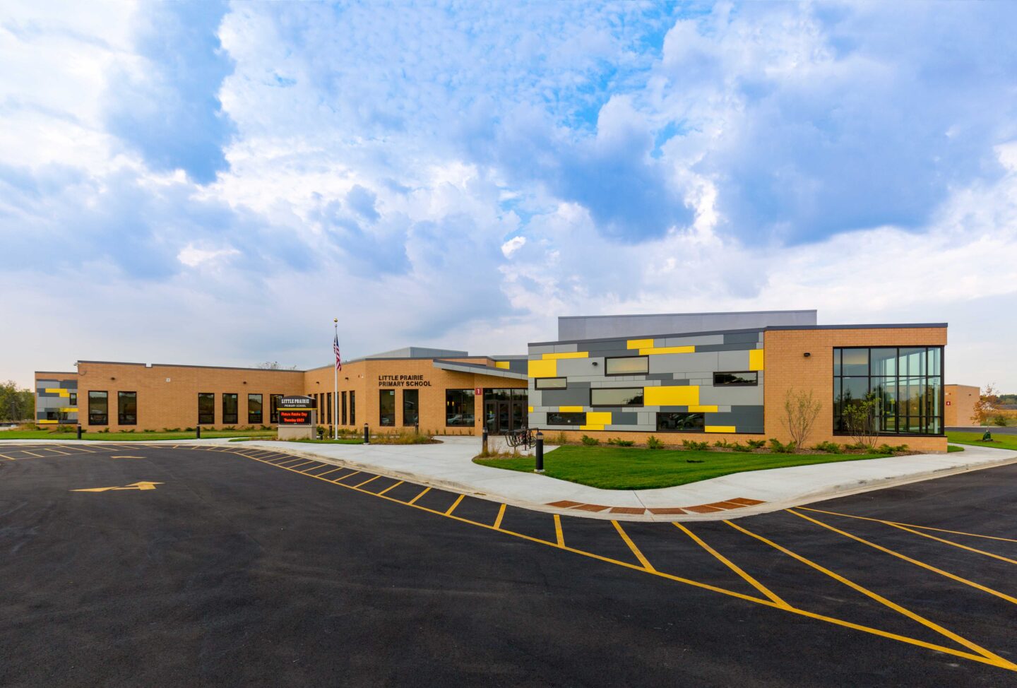 An exterior view of the school's main entry, including an accent wall of grey and yellow panels that welcomes students, staff, and visitors