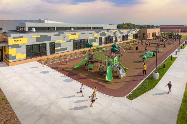 Overhead view of kids playing throughout a large playground adjacent to a school