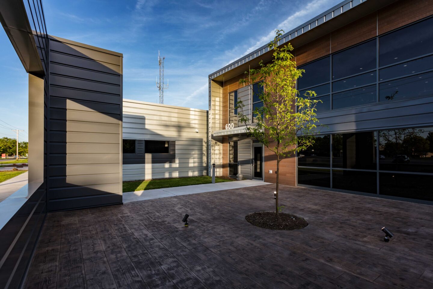A tree grows in the middle of a courtyard area that flanks the entrance of a modern police station building