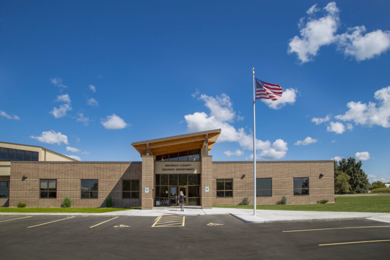 Exterior view during the day of a low building with a raised, angled roof at the entrance