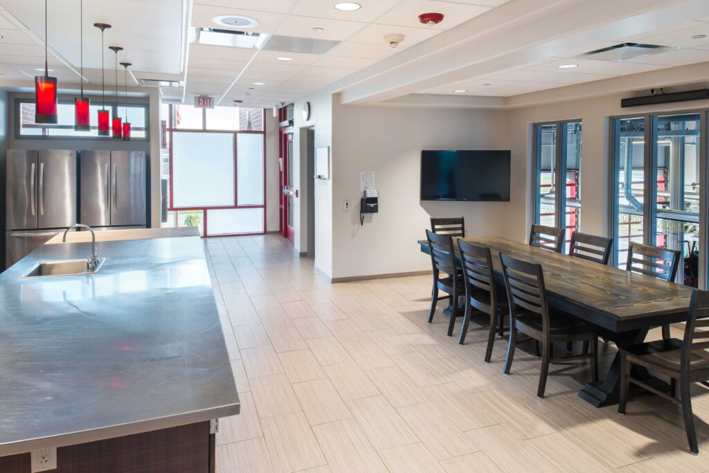 Natural light fills a red-accented kitchen connects to a large dining table at the Oak Creek Fire Station No. 1