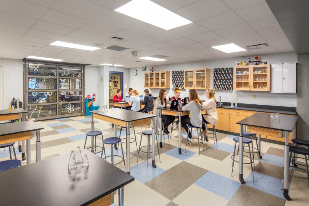 Flexible lab-height tables in a bright classroom connect to other STEM spaces with a glass garage door inside Wheatland Center School