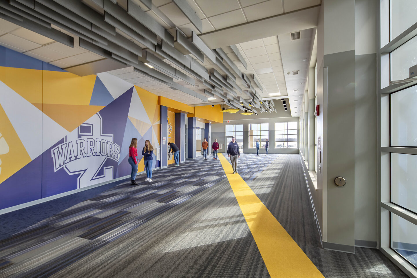 A colorful mural with school colors and logo lines a window-enclosed hallway at Northern Ozaukee School District