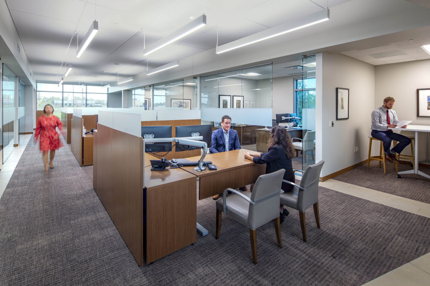 Modern workstations line an open office area leading to a wall of windows