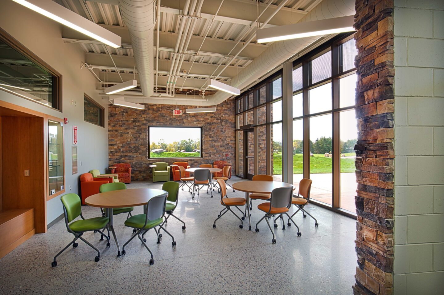 A room with tables and chairs overlooks rolling hills through a wall of windows