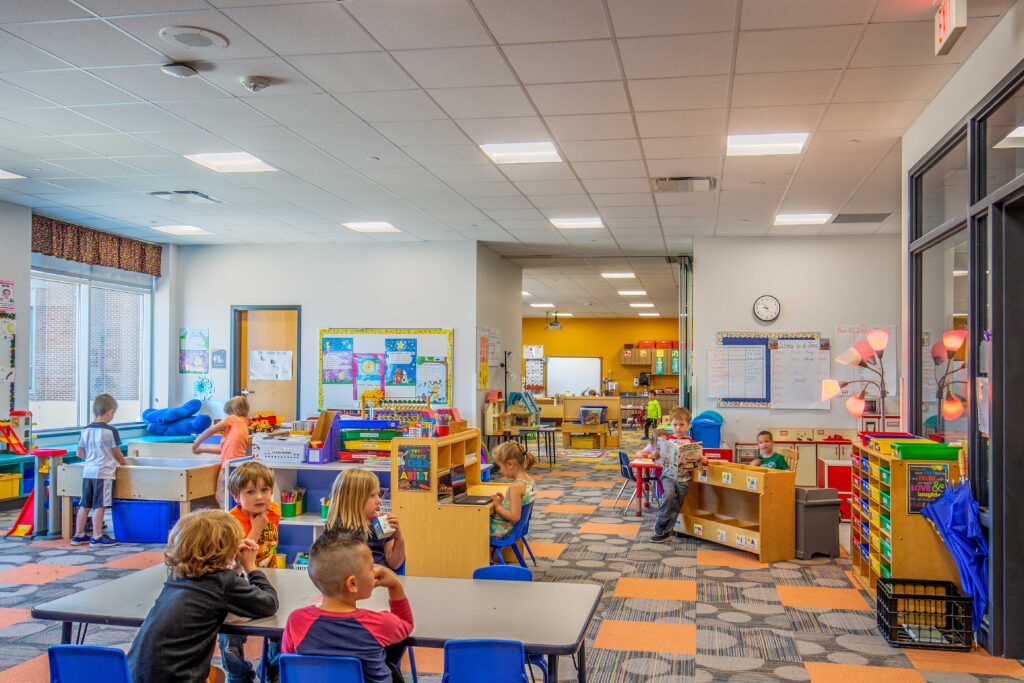 Children work and play at furniture throughout two bright, open class spaces connected by a short pass-through at Belleville Intermediate School