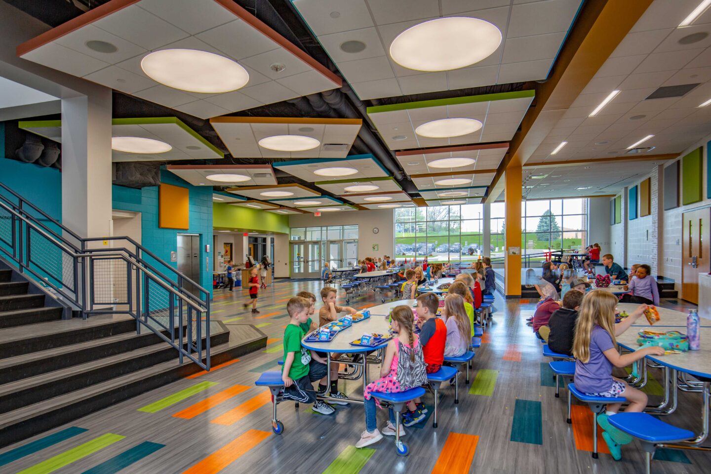 A wide staircase opens into a colorful cafeteria with a wall of windows providing natural light at Belleville Intermediate School