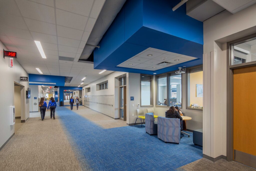 Academic corridor, featuring brand color, furniture, lockers and window into classroom.