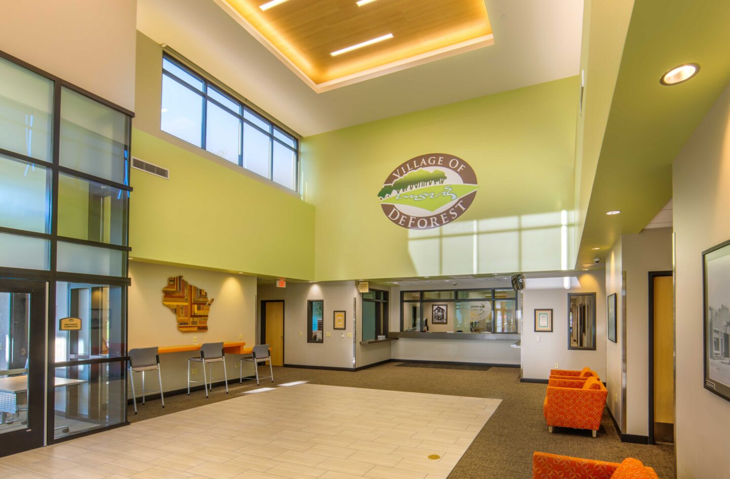 The Village of DeForest logo displays above a high-ceilinged, windowed lobby in DeForest Village Hall