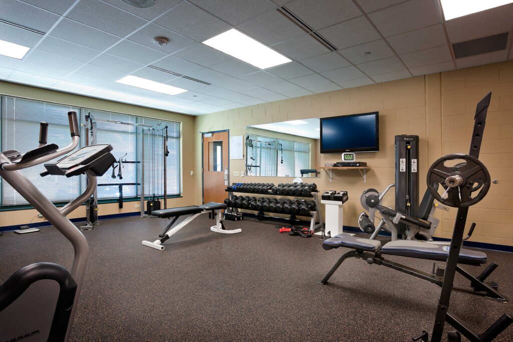 A room filled with weights and exercise equipment is lined with windows and a TV in the Delafield Public Safety Building