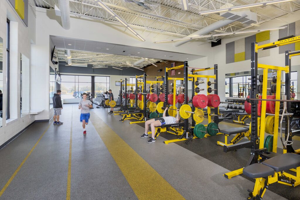 Students use weights and other fitness equipment in a large, windowed athletics area