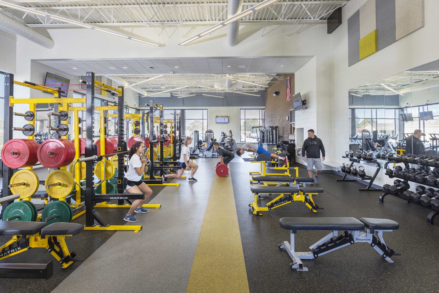 Students use weights and other fitness equipment in a large, windowed athletics area