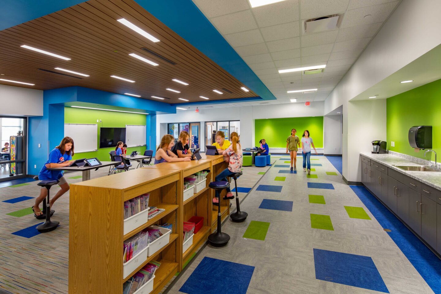 View of a collaboration space accented with bright colors that is lined with low shelves and a sink area at Eleva-Strum Elementary School