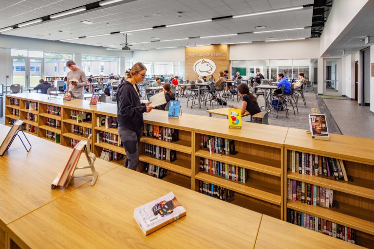 Low library shelves lead into an open study area, with a large Greendale High School logo on a far wall