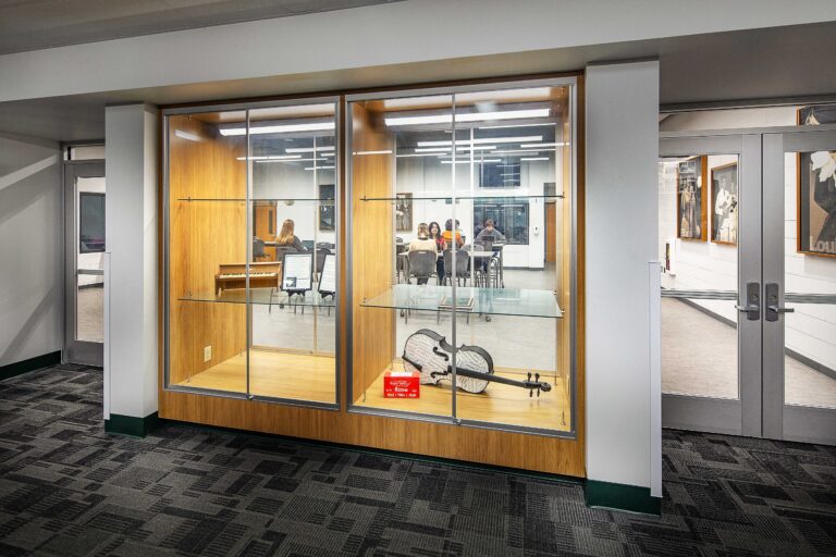 A glassed-in case peeks into a band education classroom, where students work at tables