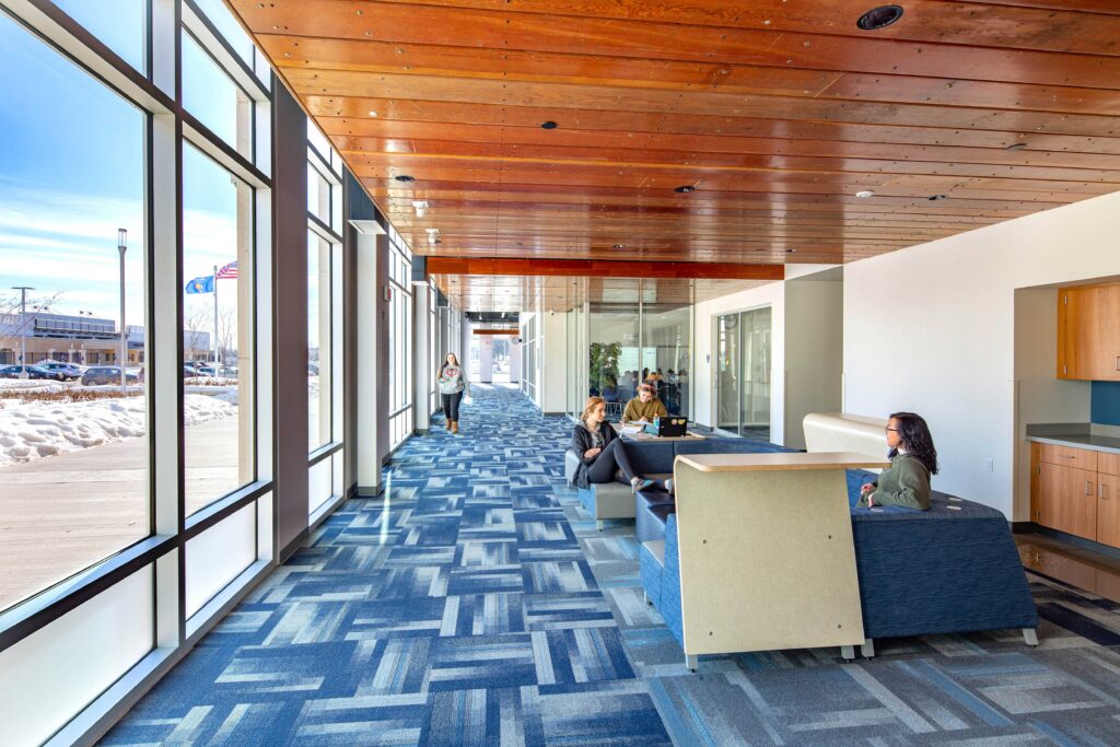 Students use flexible chairs and work surfaces for collaboration in an area connected to a windowed hall at Hudson High School