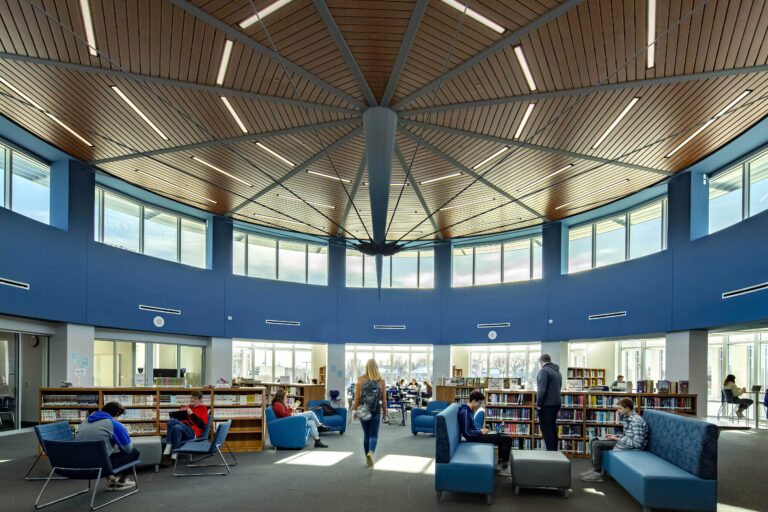 Two levels of windows illuminate a library space with a circular wooden ceiling at Hudson High School