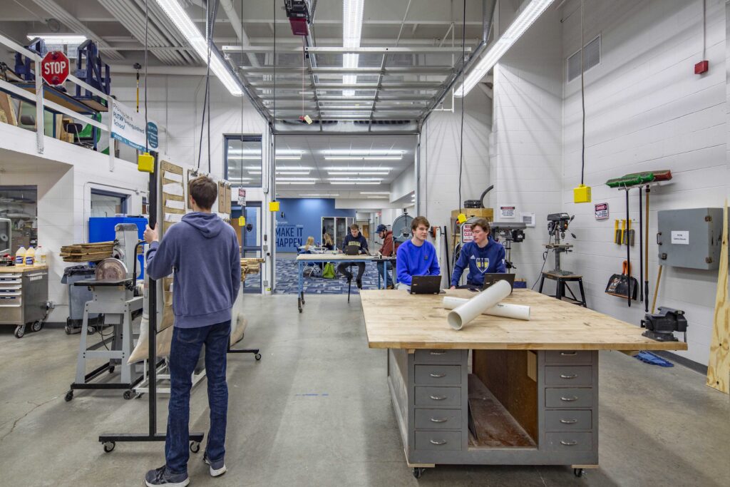 Students work around tables and equipment in a high-ceilinged STEM lab that opens into a collaborative space through a glass garage door