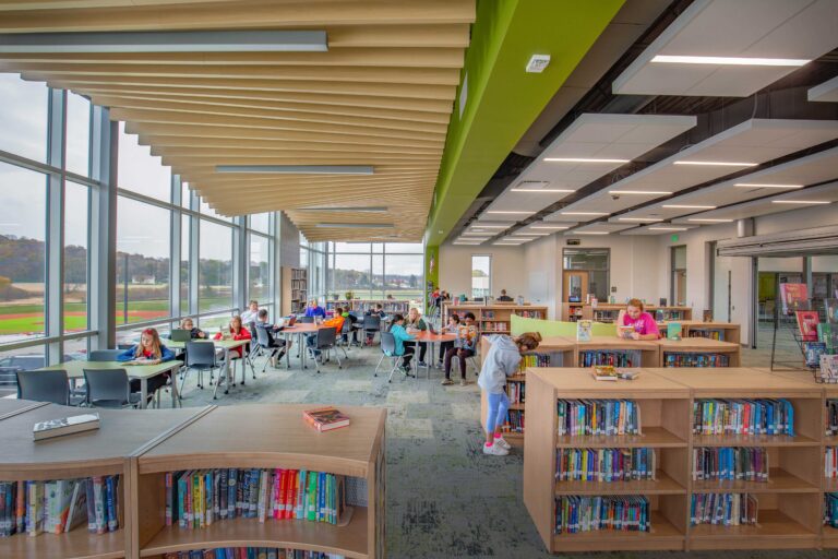 Students sit at tables near large windows in the library under an undulating canopy of acoustic ceiling panels