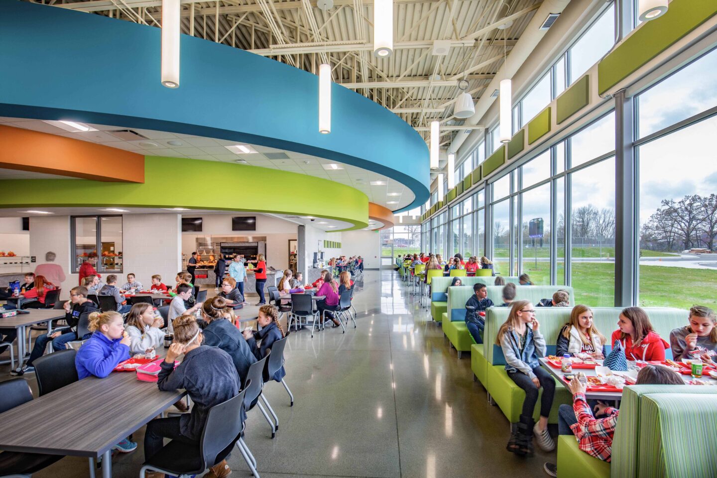 Students eat in the middle school cafeteria, which features brightly-colored soffits and a large glass curtain wall