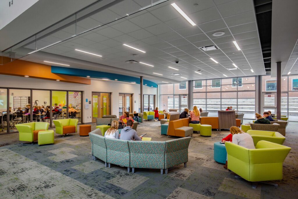 Students use the flexible furniture in the resource area with a glimpse into a nearby classroom through sliding glass partitions