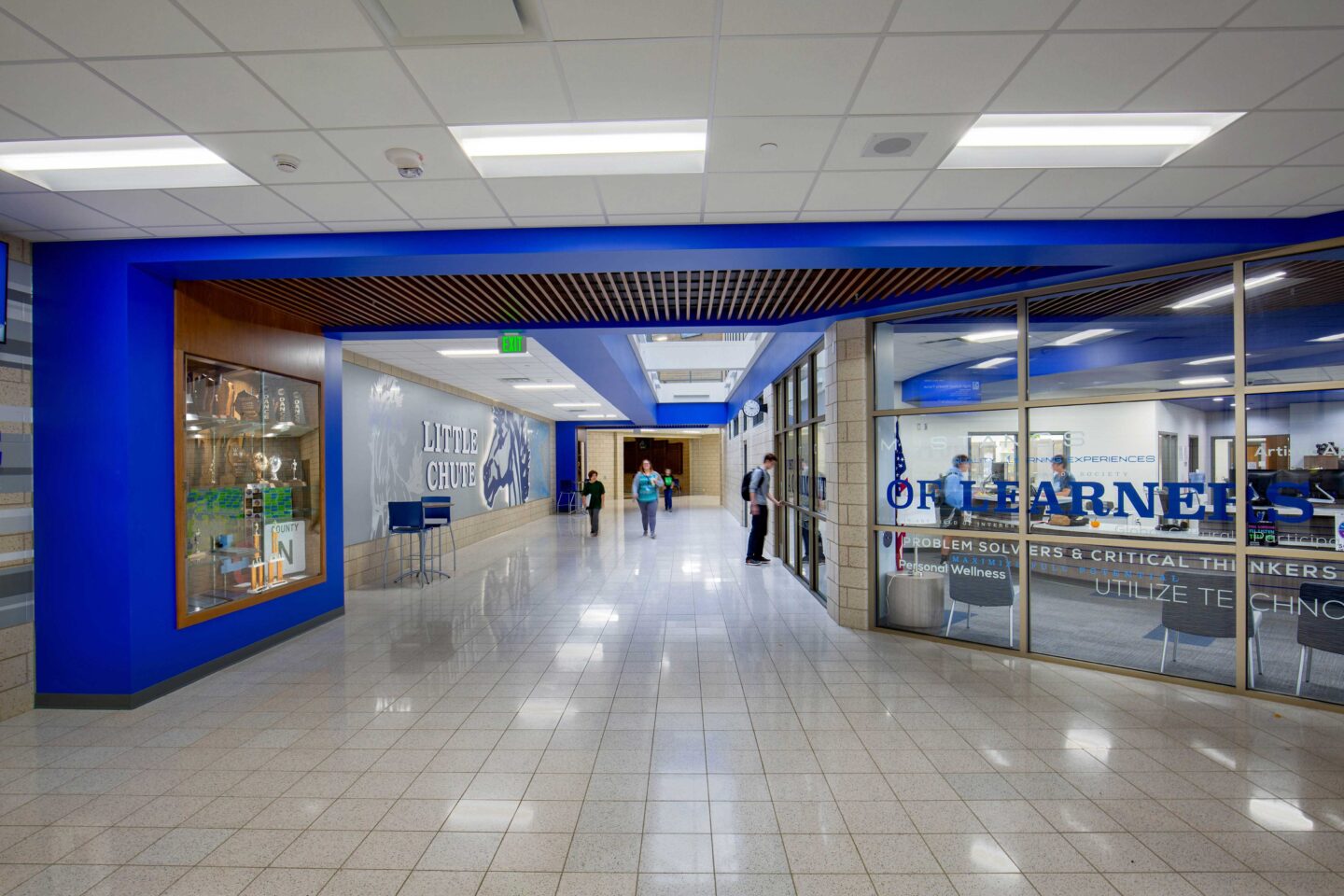 View of the entrance corridor at Little Chute Intermediate, Middle, and High School, which features display cases, a wall mural, and glass walls connecting to the office