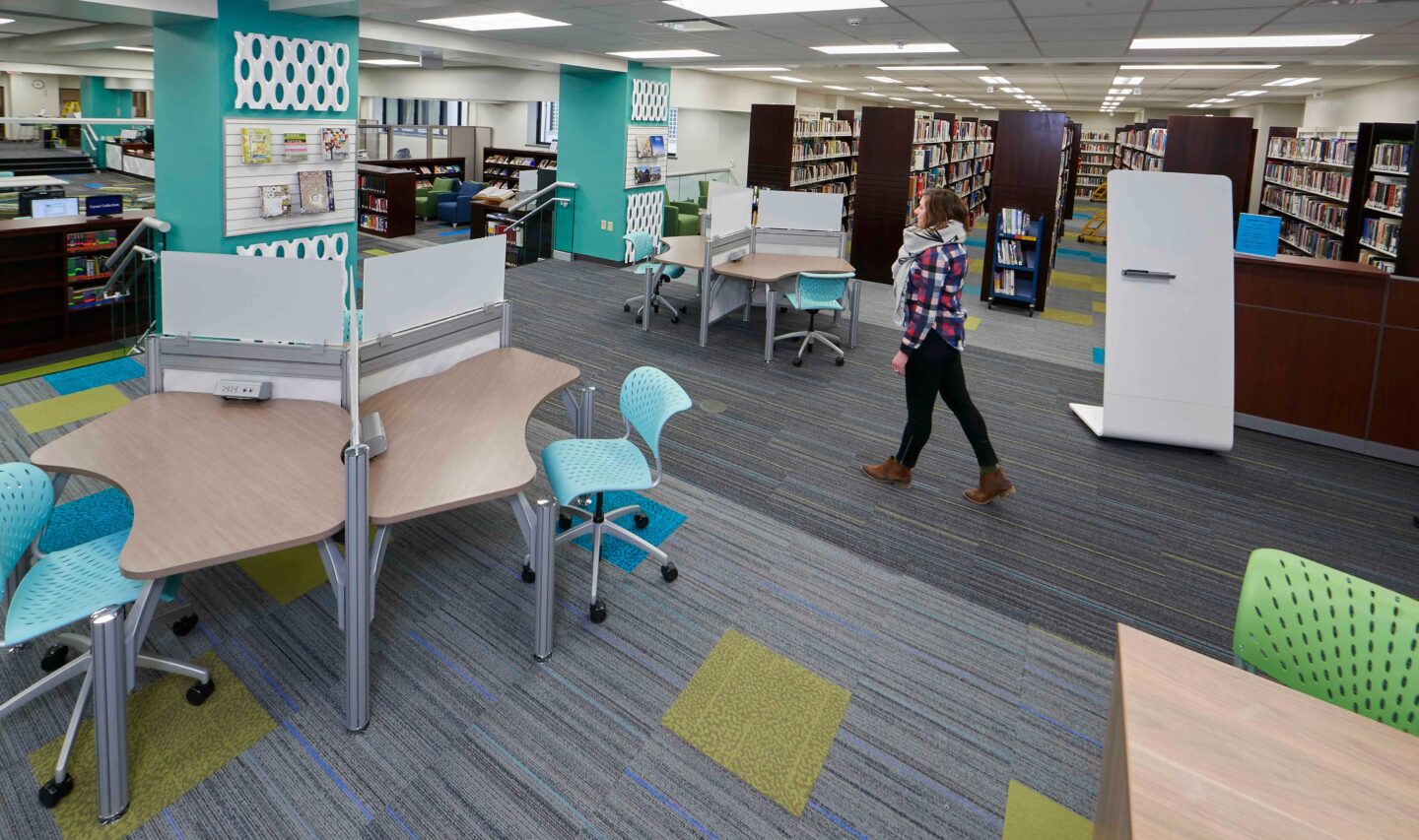 A student walks through a colorful library space with work tables and bookshelves
