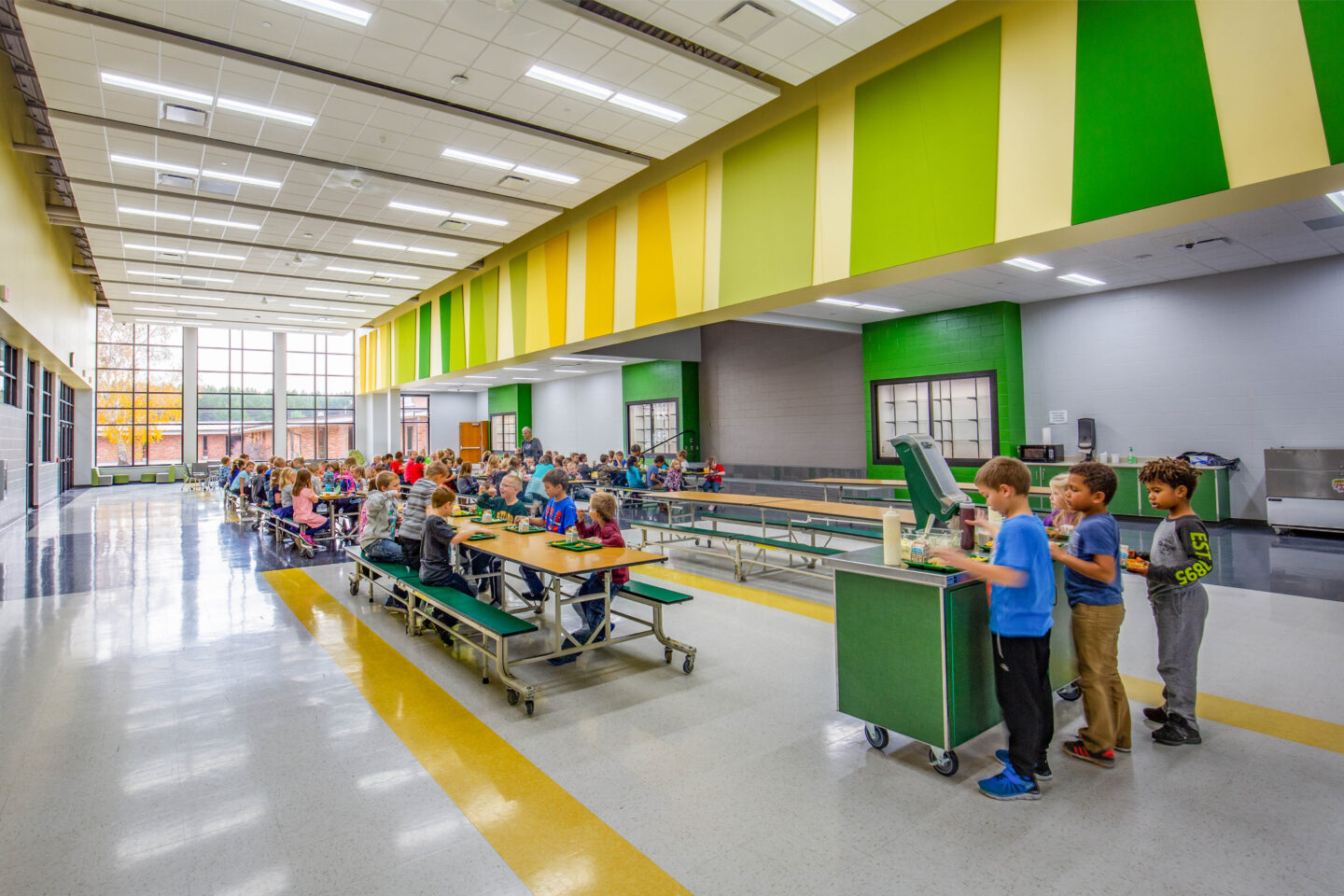 Students gather around long tables in a cafeteria filled with natural light and bright colors at Melrose-Mindoro Area School District