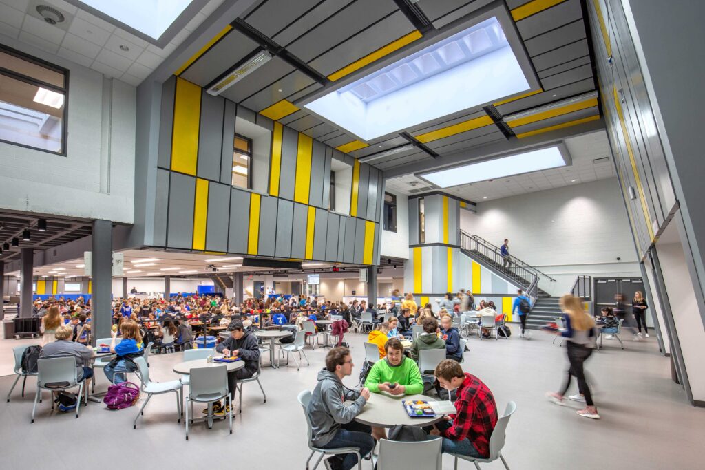 Interior view of a busy cafeteria with colorful vaulted ceilings and multiple skylights at Mukwonago High School