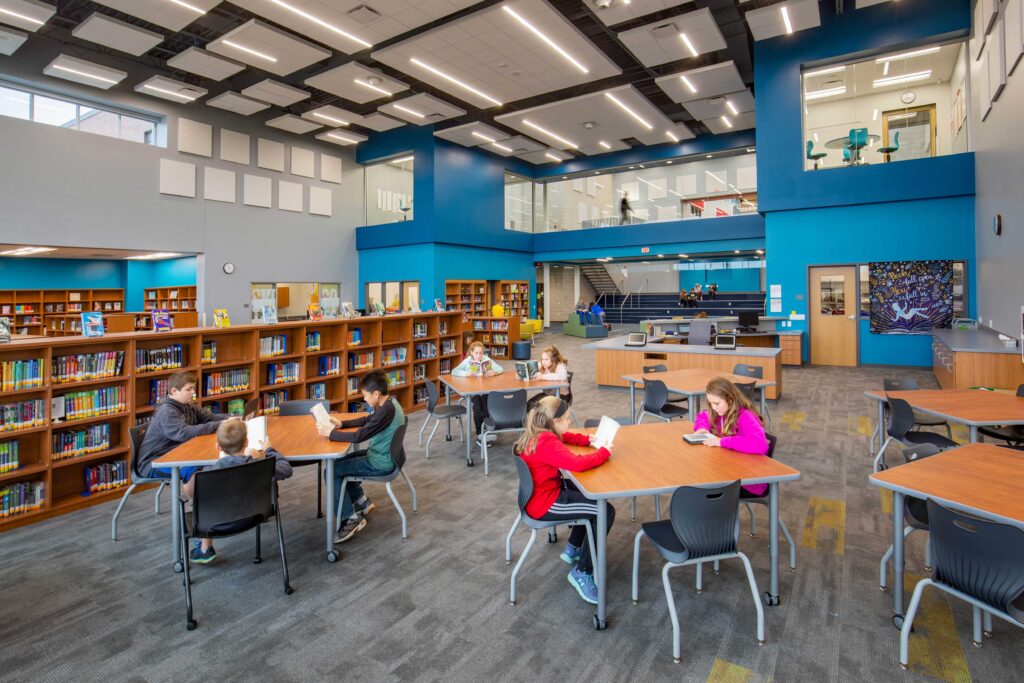 A view of the library with tables, book stacks, and windows that overlook the library from second-floor meeting rooms and hallway