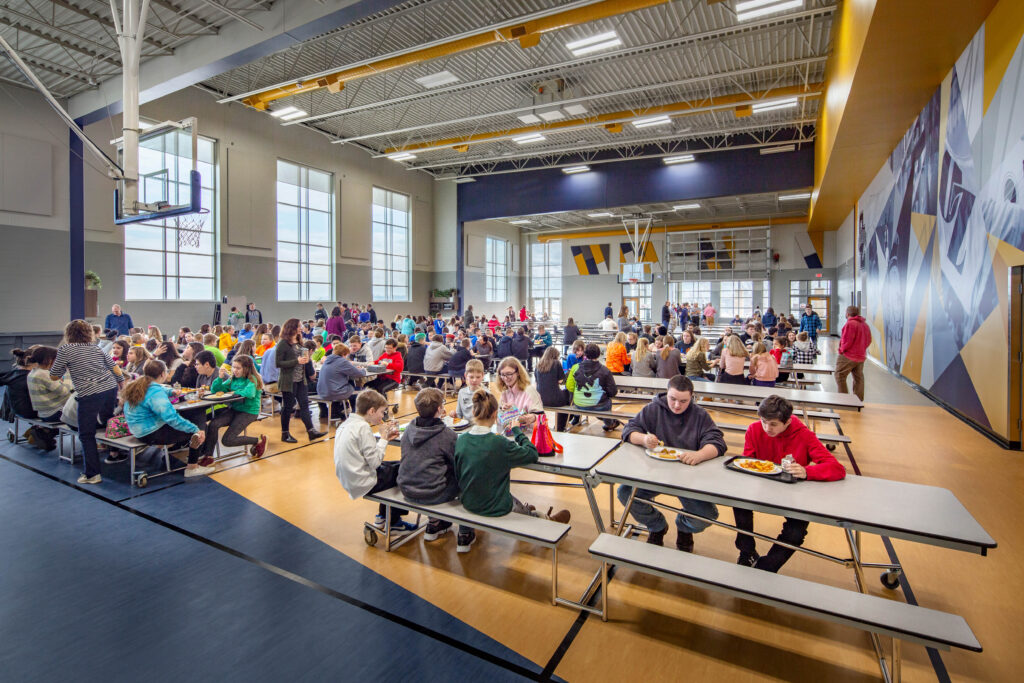 Basketball goals hover above filled tables in bright, multipurpose cafeteria at Northern Ozaukee School District