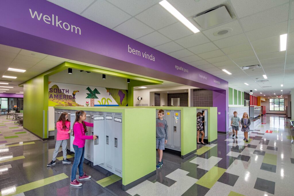 Students visit their lockers, which are near colorful environmental branding installations that feature information about the world's continents