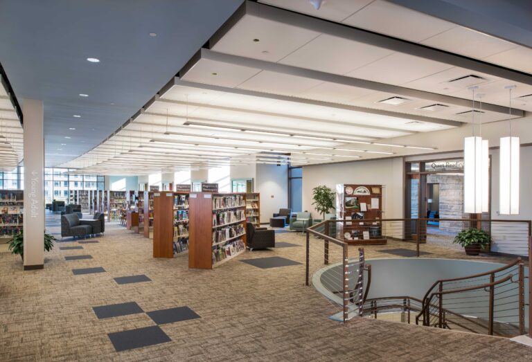 Light from a wall of windows floods the upper level of a library reached by a circular staircase at Oak Creek City Hall and Public Library